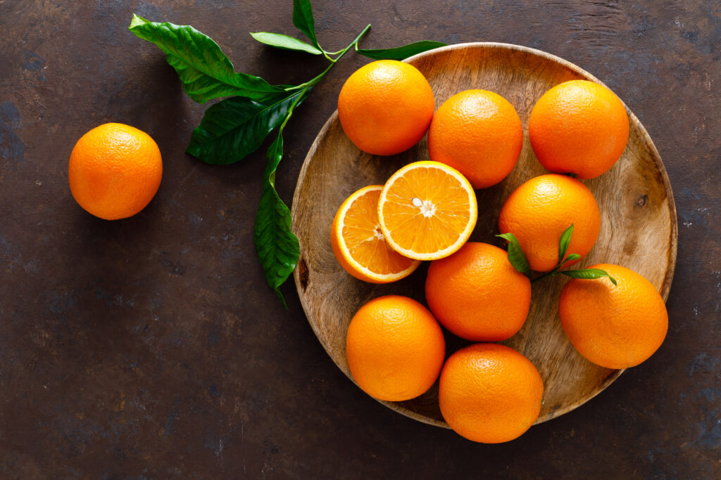 A wooden bowl filled with oranges on top of a table.