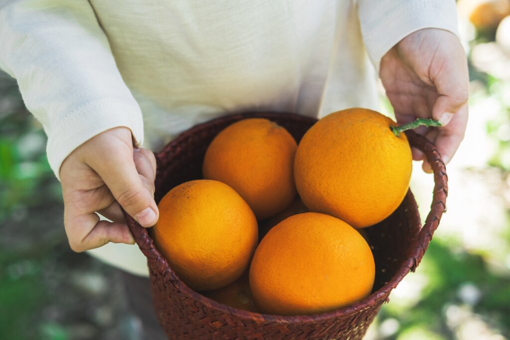 A person holding a basket full of oranges.