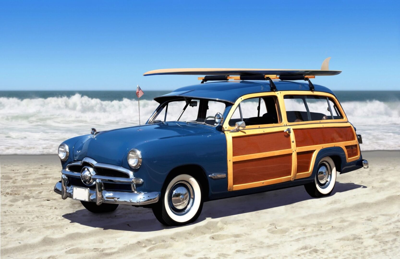 A picture of a classic wagon car at the beach with surfboard onto of the car.